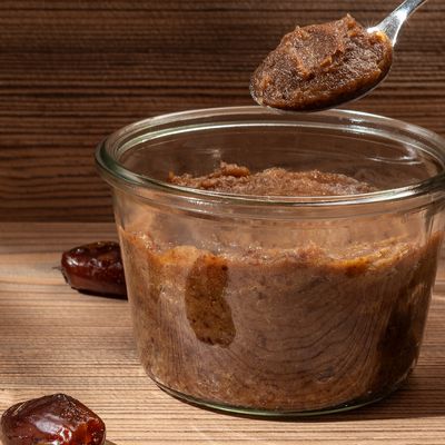 Eine Hand hält einen Löffel der über der Dattelpaste ist Eine Hand hält einen Löffel der über der Dattelpaste ist