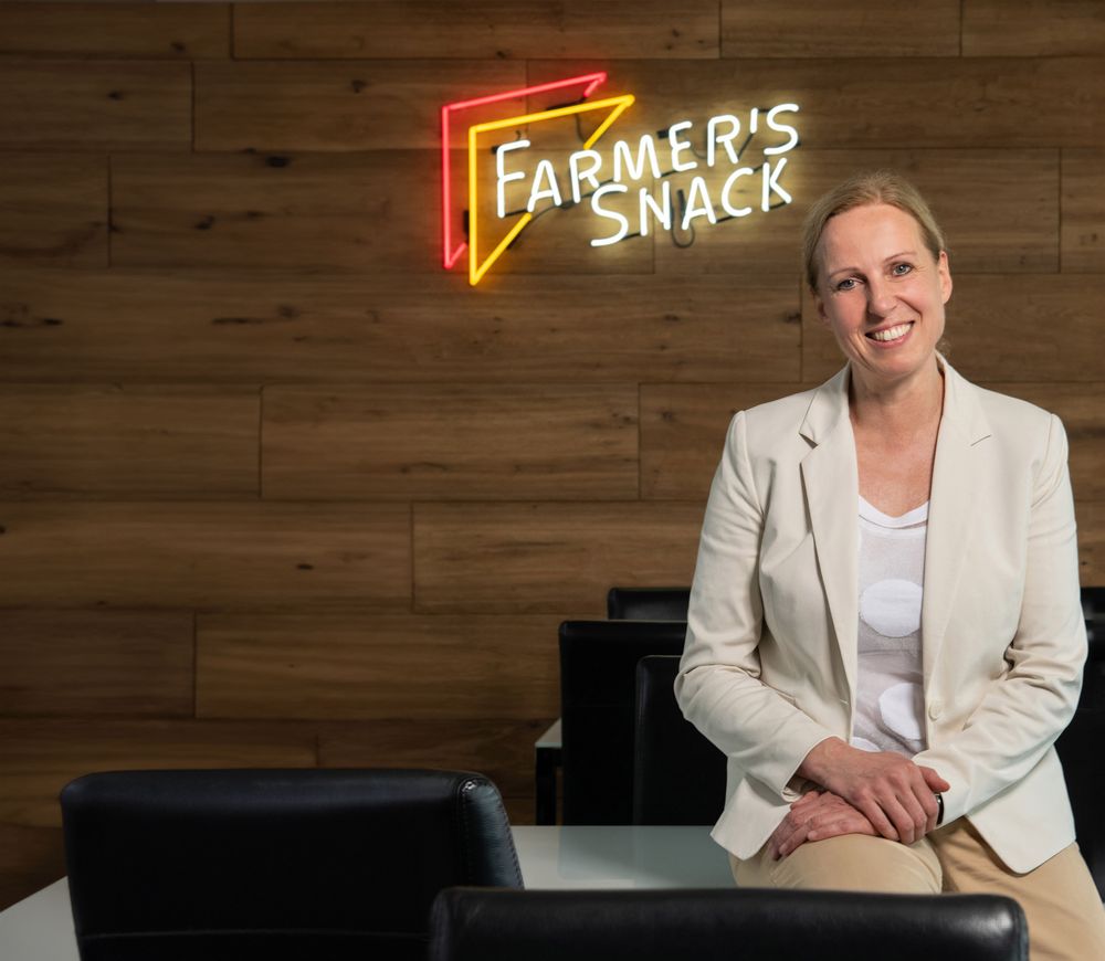 Cornelia Ahrens sitzt auf einem Tisch vor dem Farmers Snack Leuchtlogo